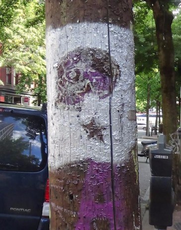 a stylized skull painted in silver on a utility pole with many old staples